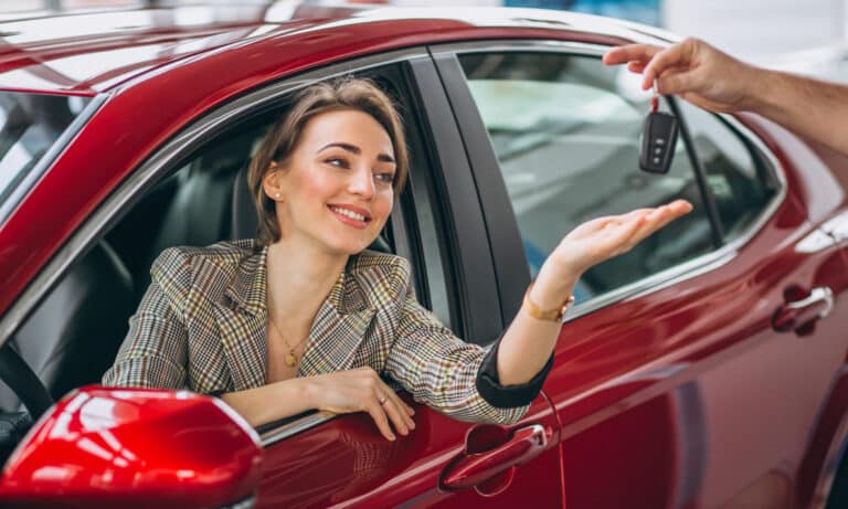 Woman sitting in red car and receiving keys for rent a car jafilliya
